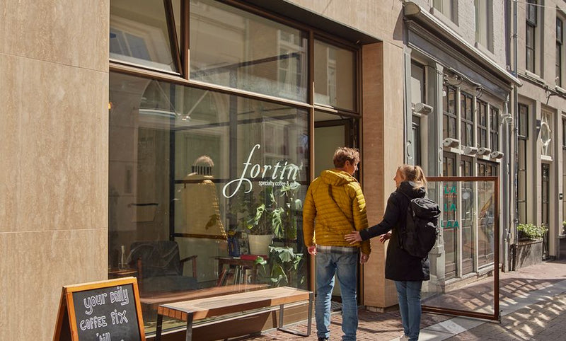 Two people standing outside Fortin Specialty Coffee Bar on a city street.