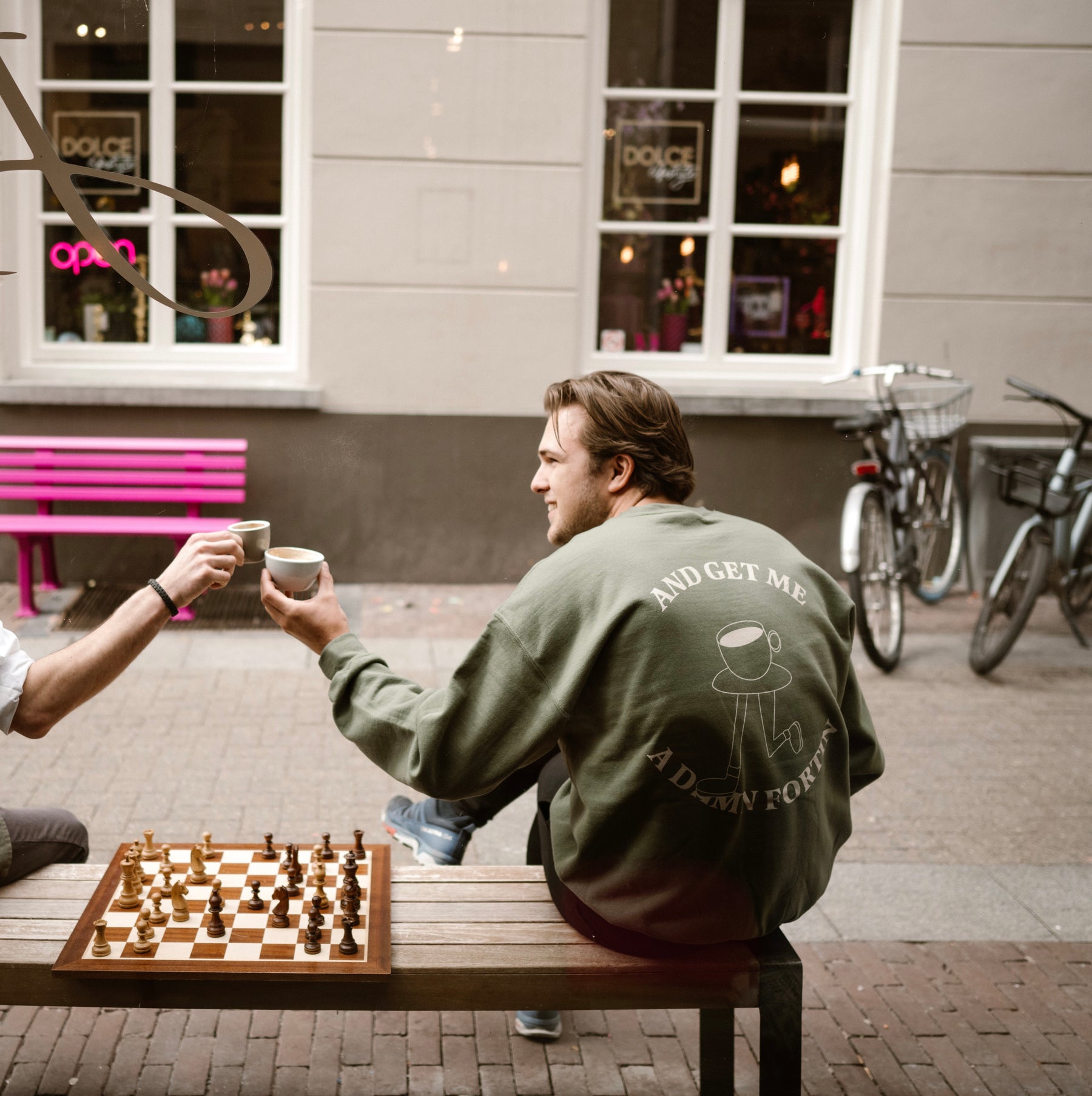 Fortin Employee Enjoying a Cup of Espresso in Den Bosch, wearing a Green Fortin Sweater and toasting with his cup.