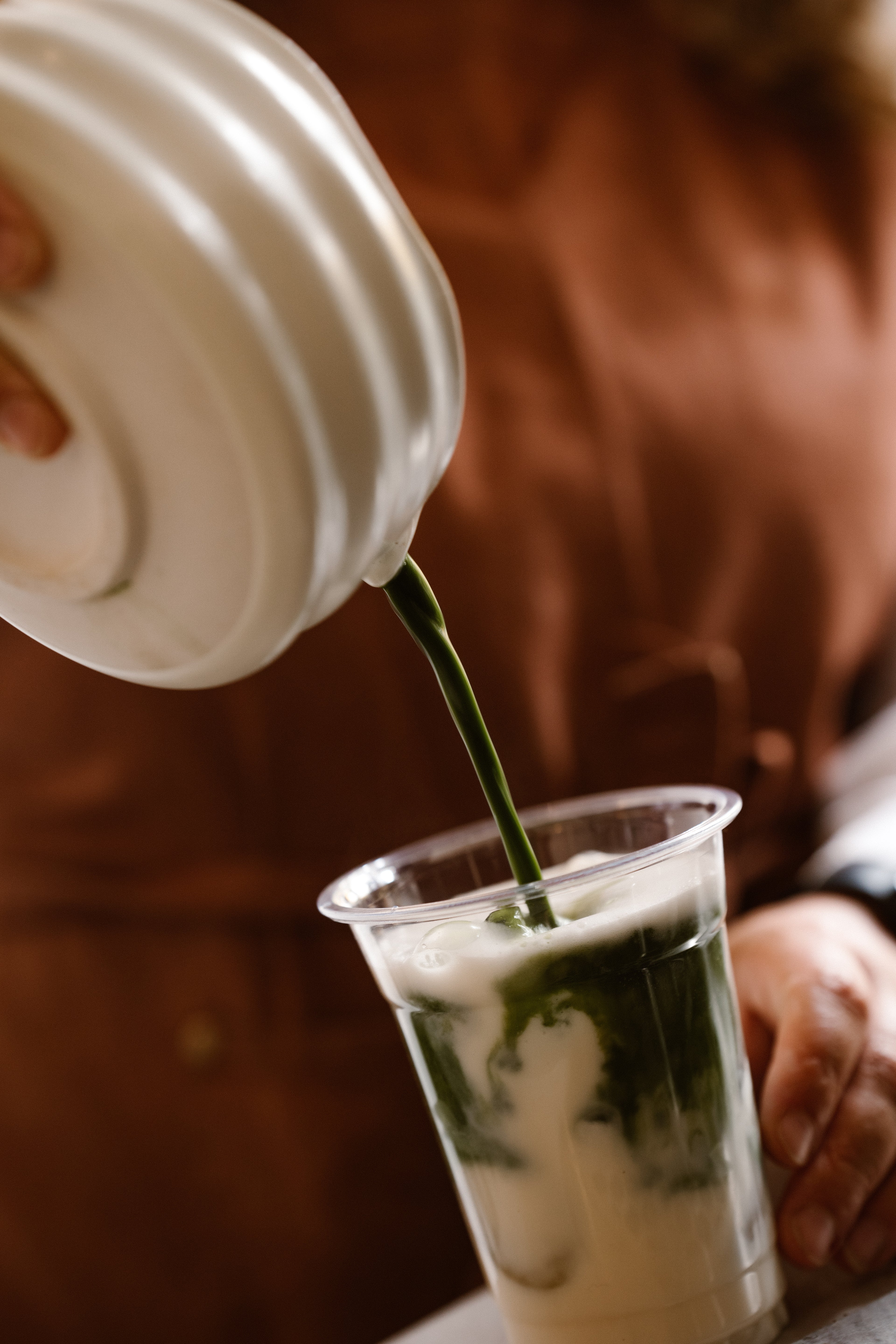 Fortin Barista pouring a matcha from a white container into a clear cup with milk